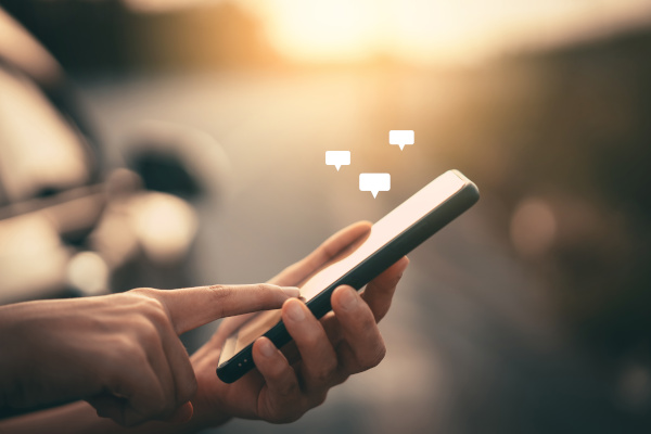 Eine Person hält ein Smartphone und tippt darauf, während Sprechblasen mit Text erscheinen.