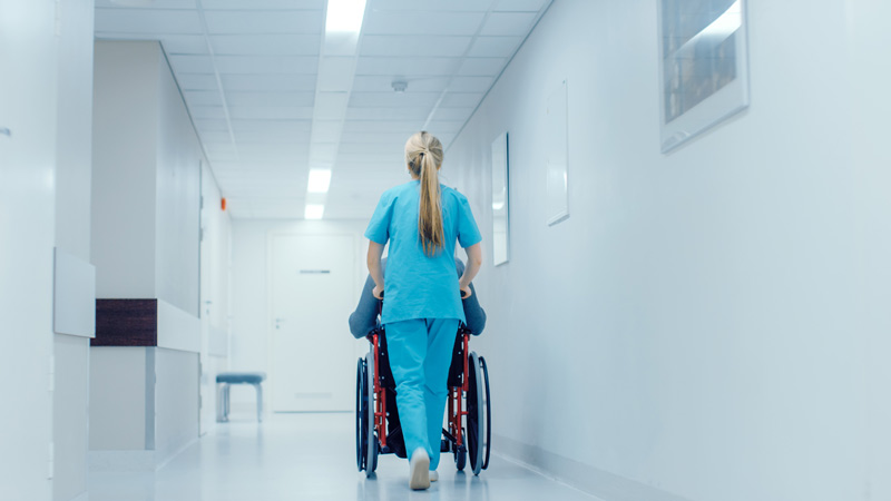 Eine Pflegekraft schiebt einen Rollstuhl in einem hellen Krankenhausflur.